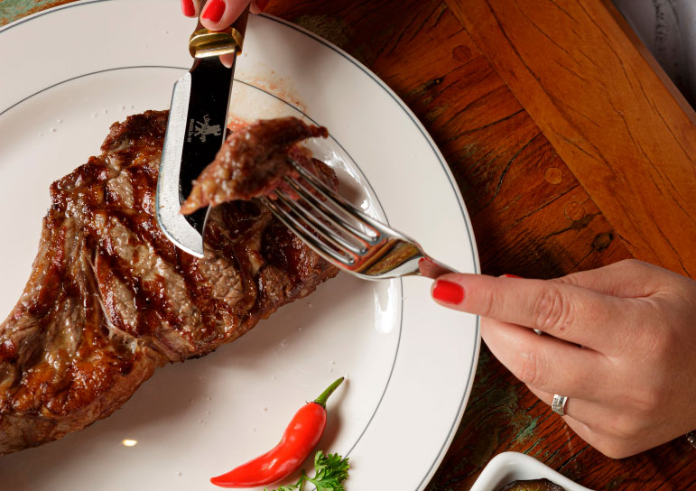close up image of a woman cutting into a steak