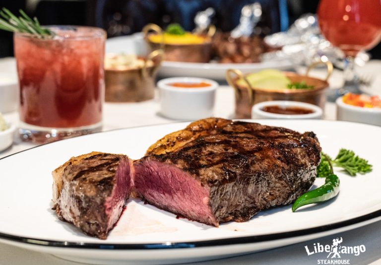 Mid-rare teak on a white plate with drinks in the background.