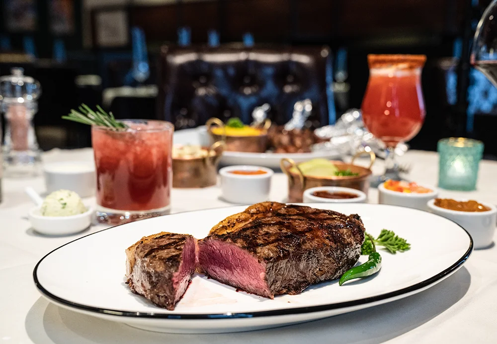 a beautifully cooked steak with drinks and condiments in the background